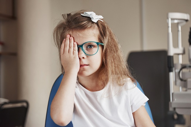 Child closes the right eye with his hand and trying to read the words on the board